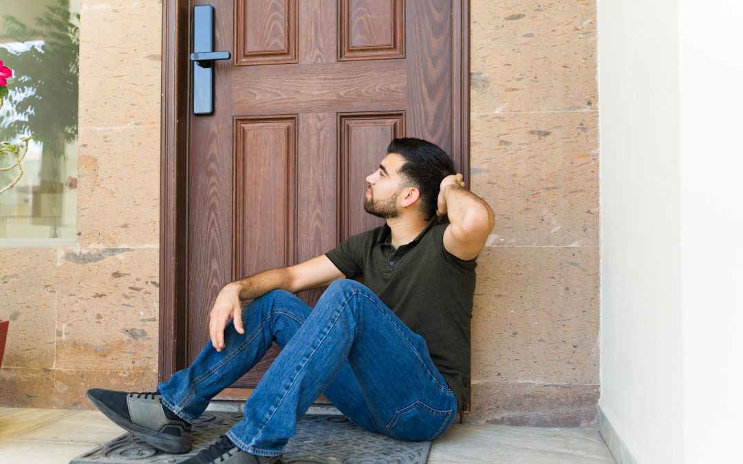Man sitting on a doorstep, looking up, with one hand behind his head and another resting on his knee.