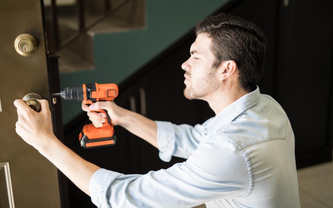 A man uses an electric drill to fix or install a door lock inside a building.