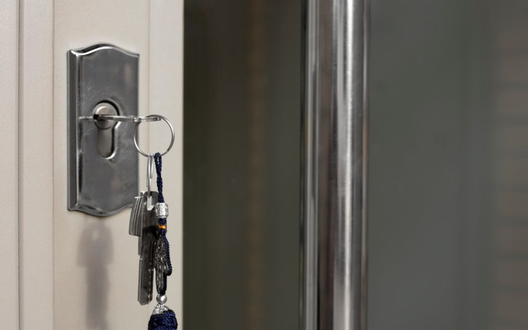 A set of keys with a keychain hanging from a door lock in a closed door.